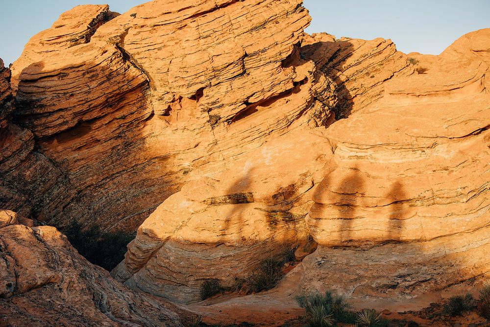 Scenic desert landscape with orange sandstone rock formations under a bright blue sky at sunset.