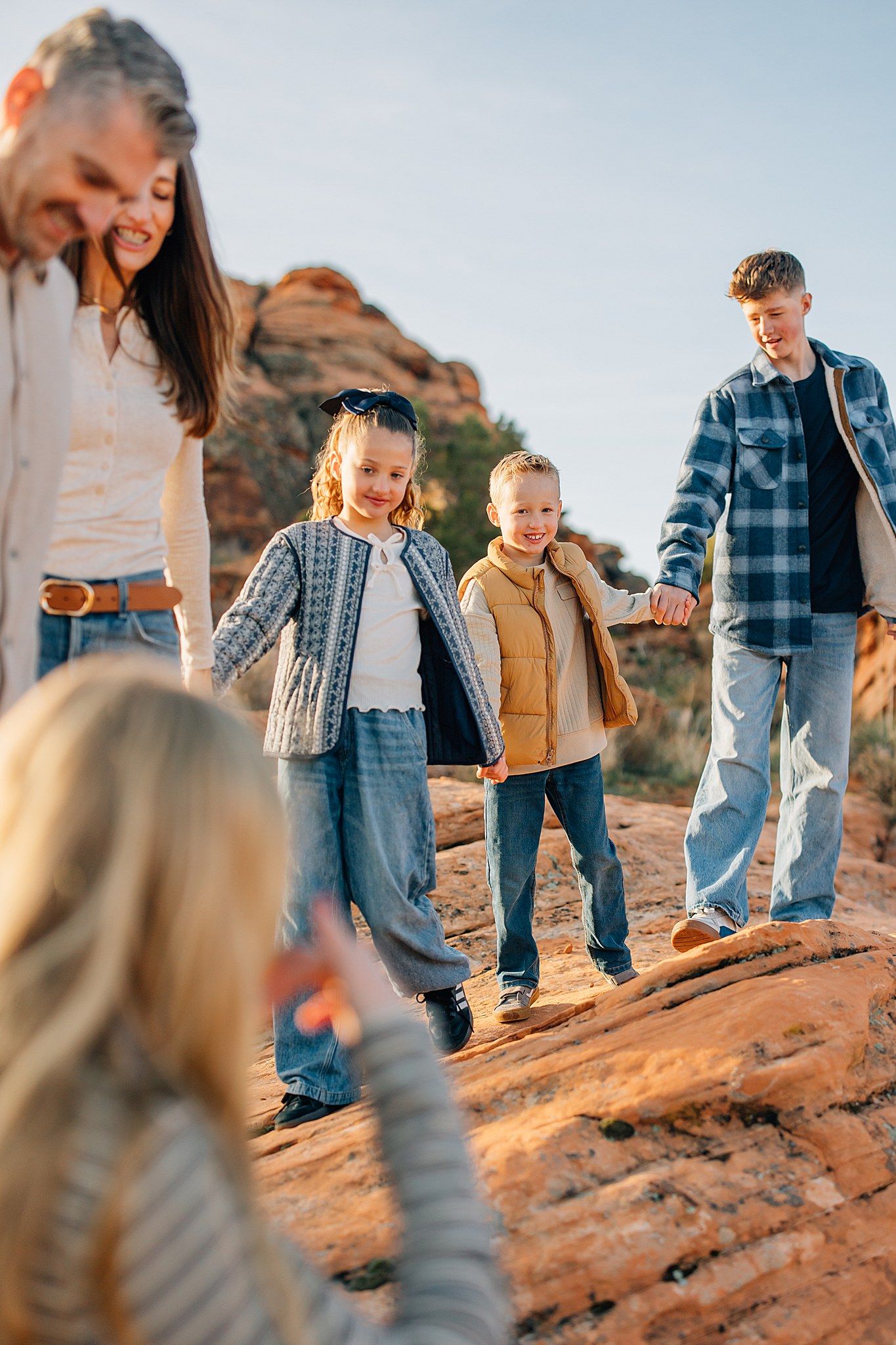 Family walking together on red rock formations during golden hour wearing coordinated blue and tan outfits.