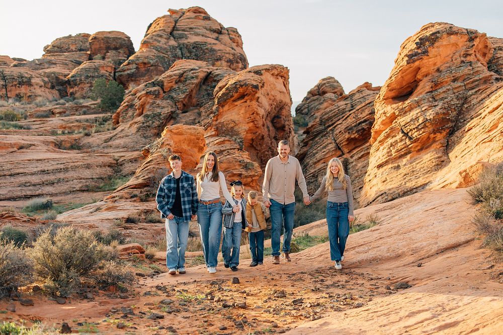 People exploring winding path through vibrant orange sandstone formations in desert terrain.
