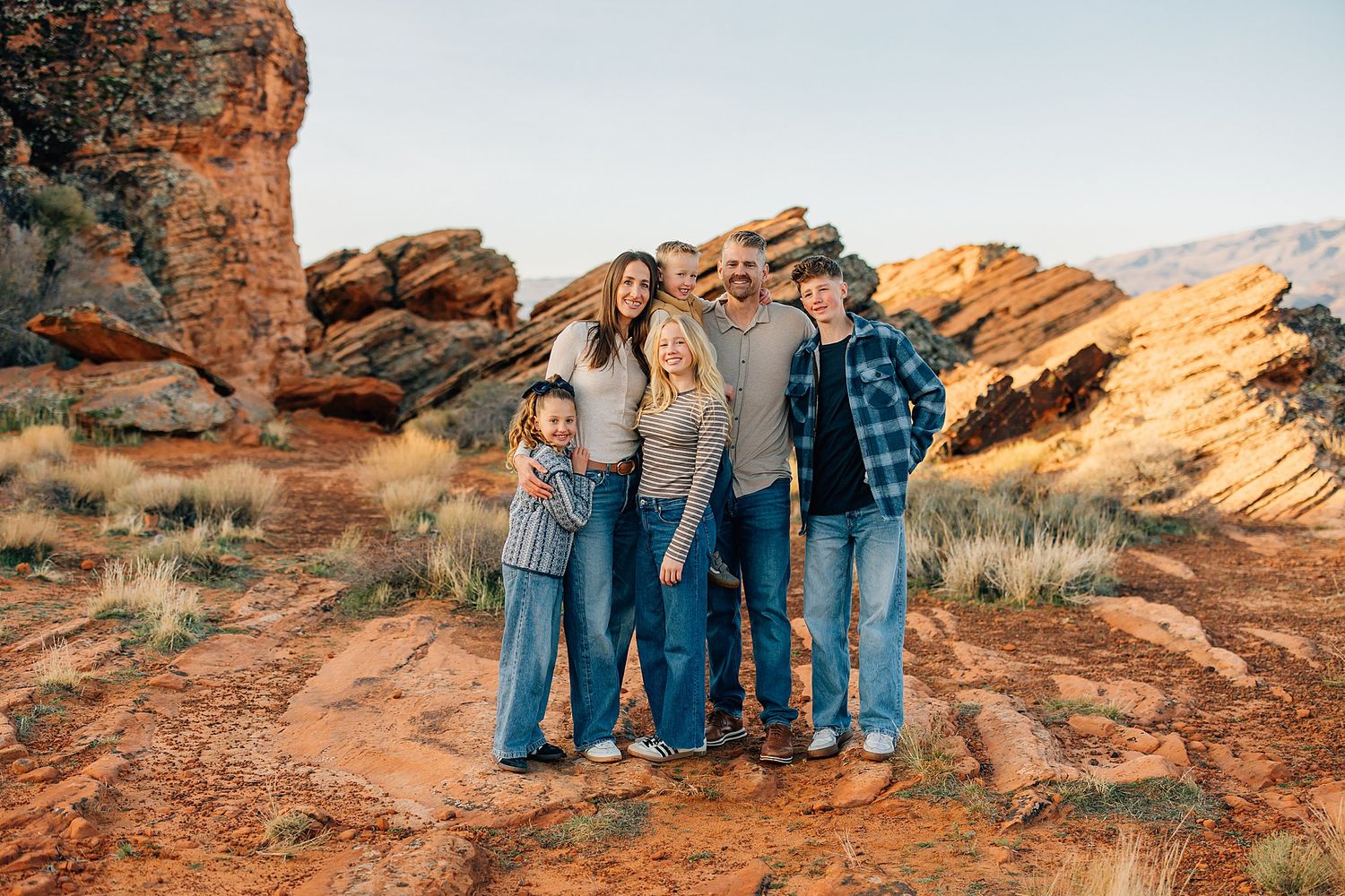 Group walking along scenic red rock formations in desert landscape during golden hour sunset.