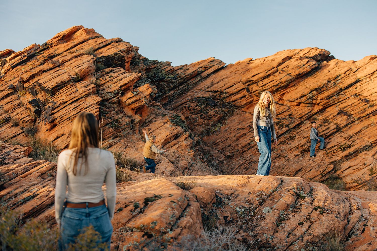 A person stands on orange sandstone rock formations at sunset, creating a silhouette against the warm desert landscape.