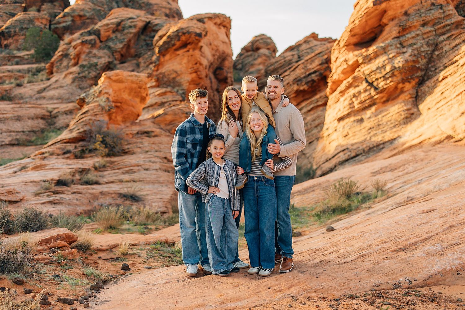 People sitting on red rock formations in a desert landscape during golden hour.