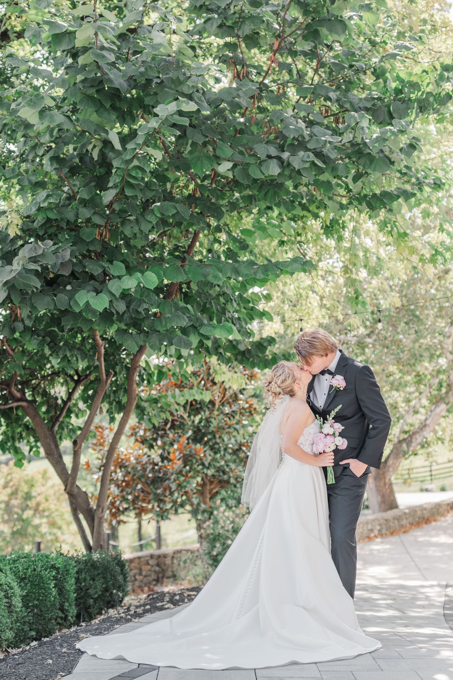 A romantic wedding photo showing a couple in an intimate moment under green trees.
