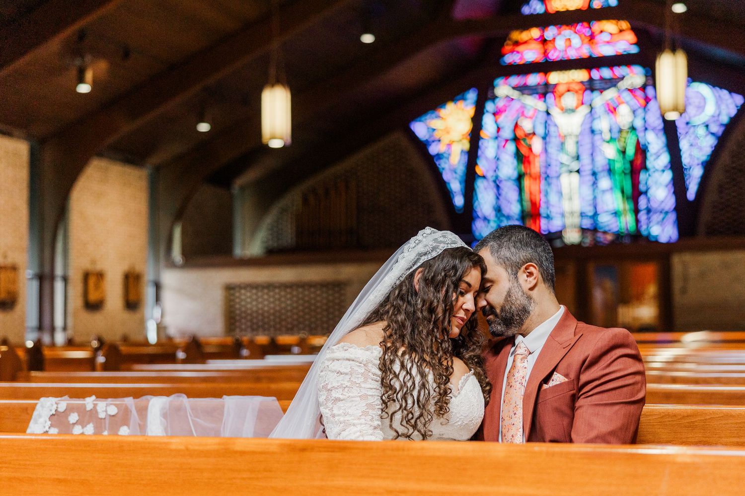 A couple shares an intimate moment in a church pew with stained glass windows visible in the background.