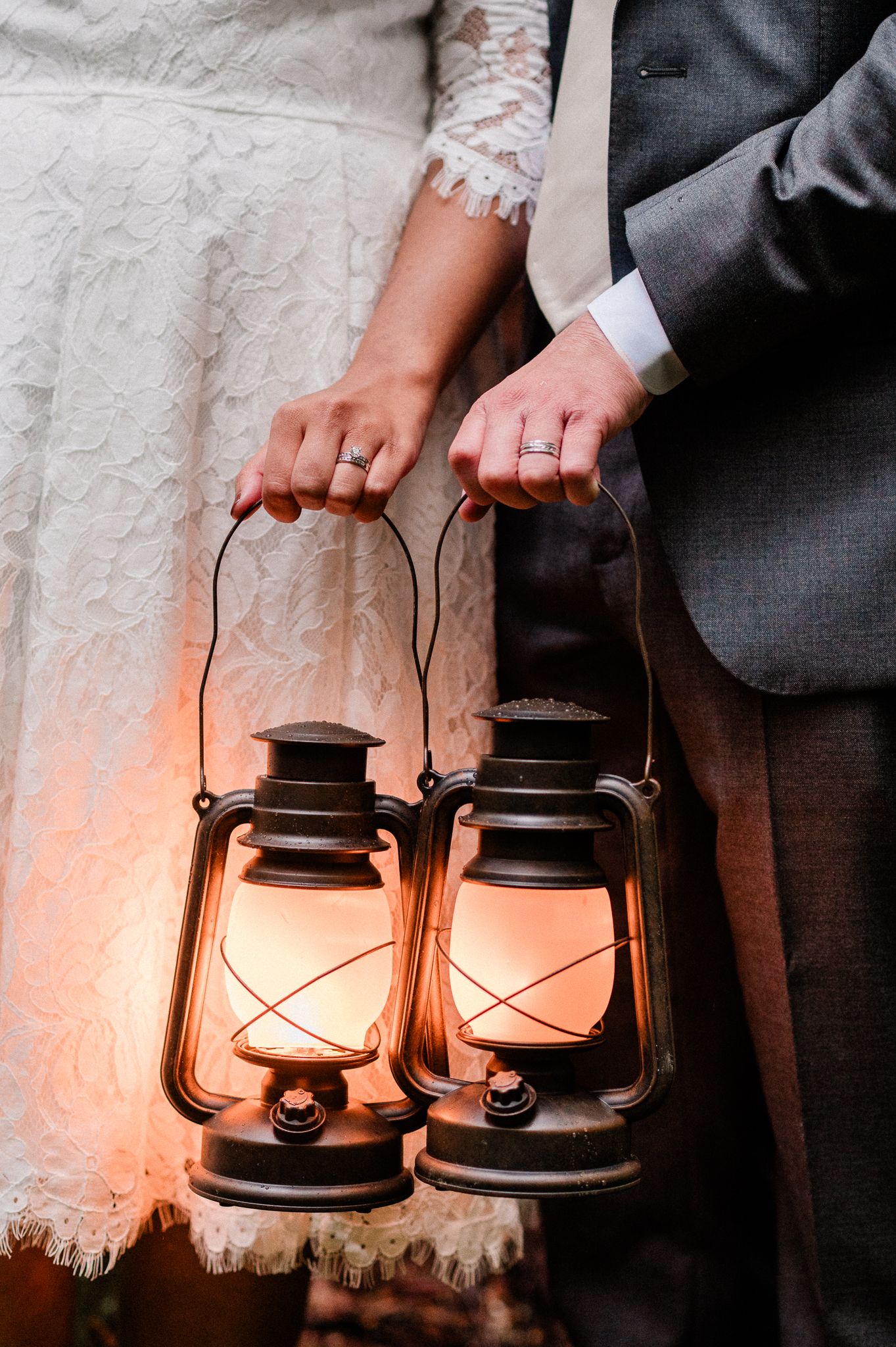 Close-up of hands holding vintage lanterns showing off their wedding rings