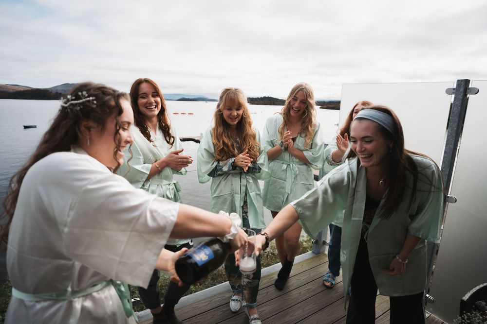 Group of people gathered on a deck overlooking water while enjoying drinks and conversation.