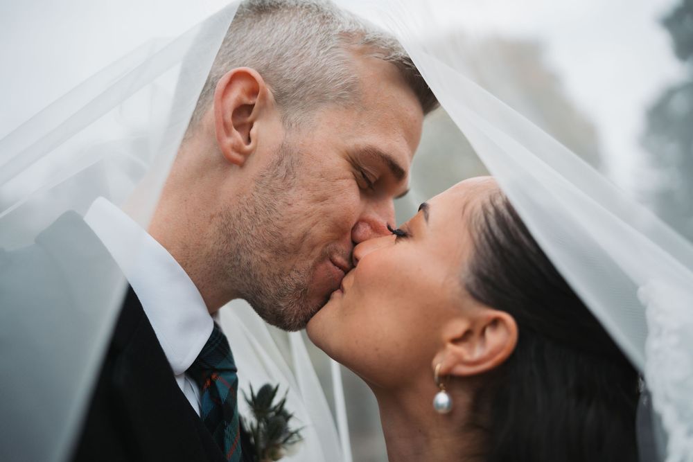 Romantic wedding photo series showing tender moments between newlyweds with flowing veil in outdoor setting.
