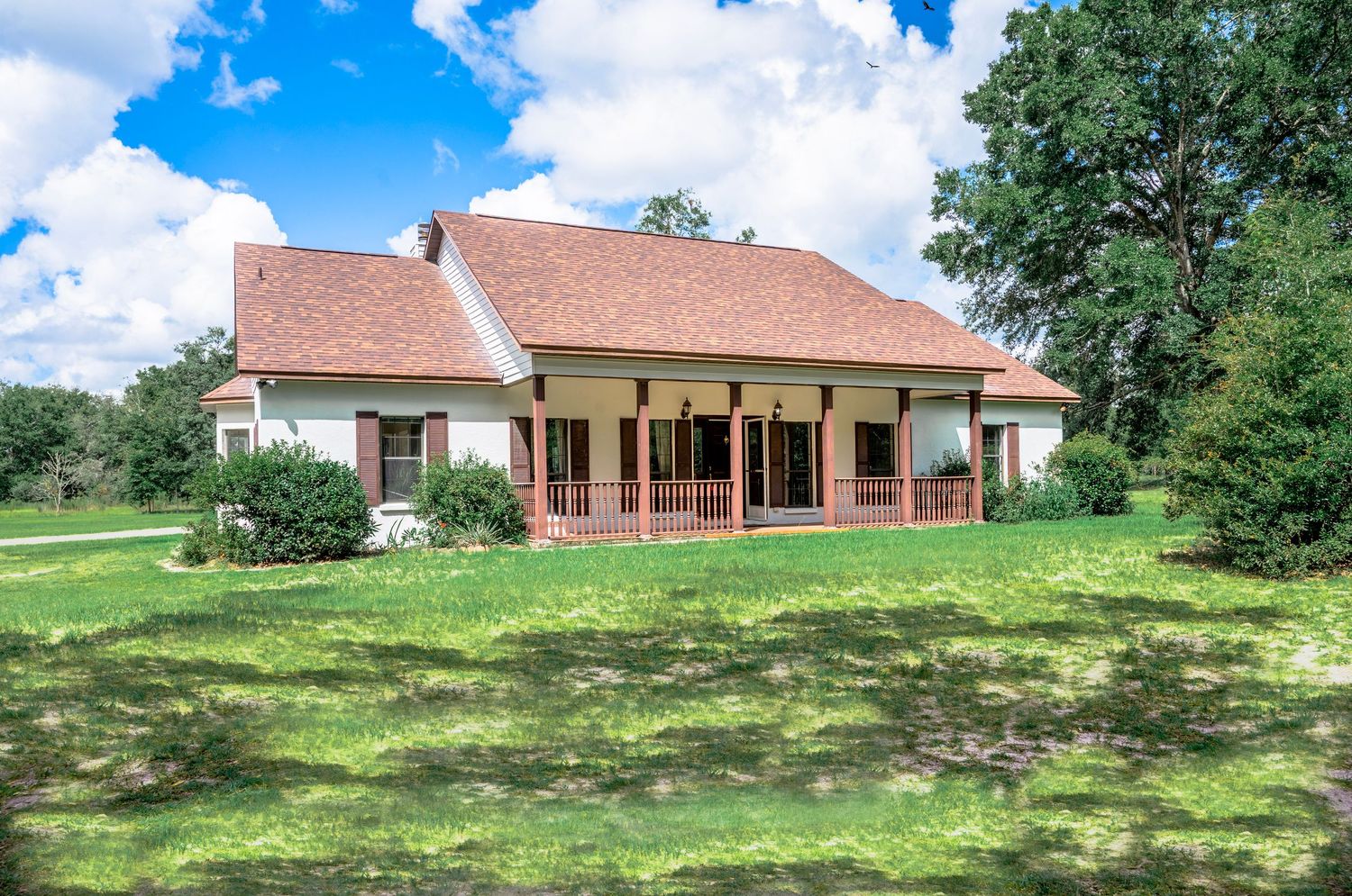 Panoramic view of a brick house nestled on a grassy hillside with trees and blue sky in the background.