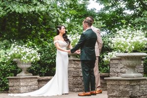 A couple shares a romantic moment in a garden setting with blooming white flowers and stone walls.