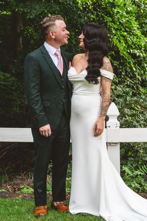 Wedding couple in white dress and dark suit sharing playful moments outdoors with greenery in background.
