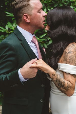 A tender moment between newlyweds as they embrace, with the bride in white and groom in emerald green suit.