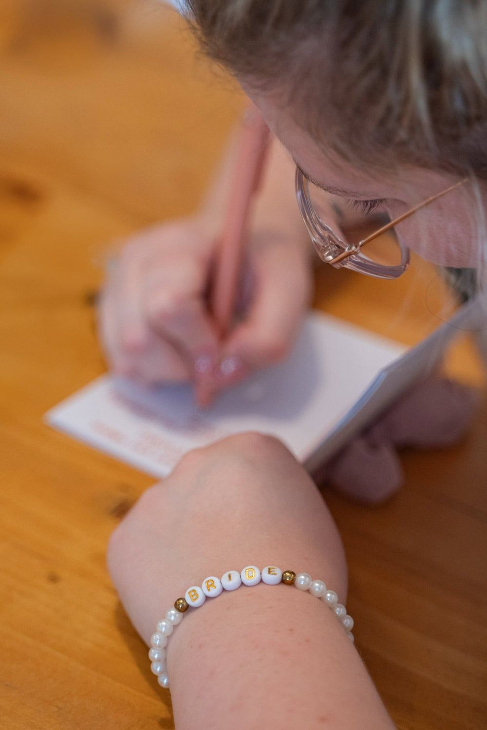 Hands writing on paper with personalized letter bead bracelet visible.