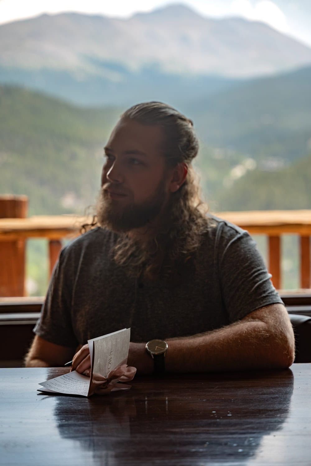Person resting on wooden table with mountain landscape visible through window in background.