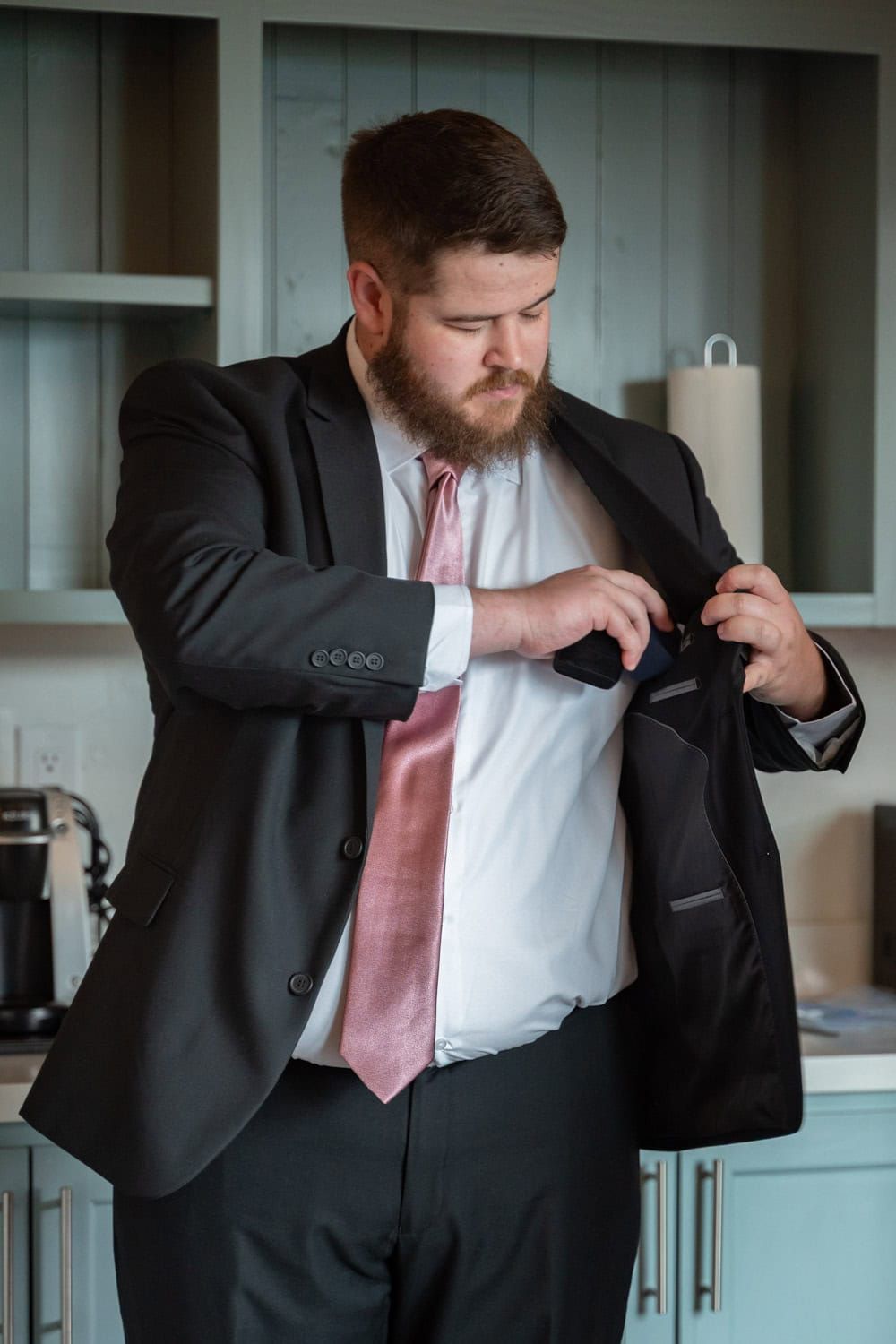Person adjusting formal black suit jacket and pink tie while getting dressed.