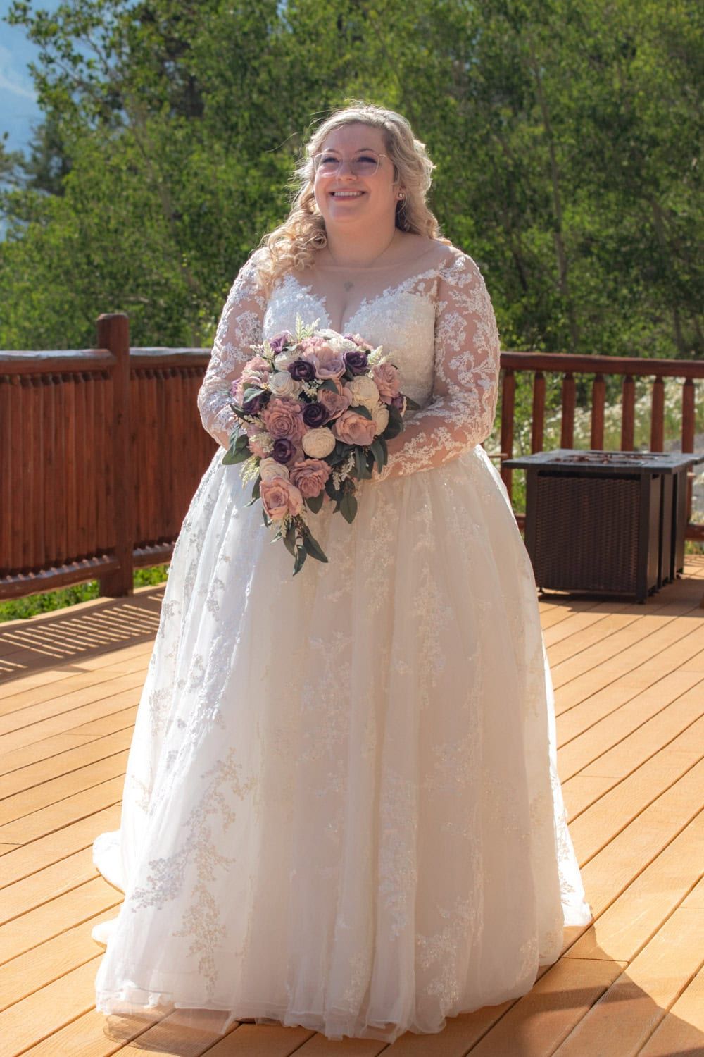 Wedding dress with lace details and pink floral bouquet photographed on wooden deck.