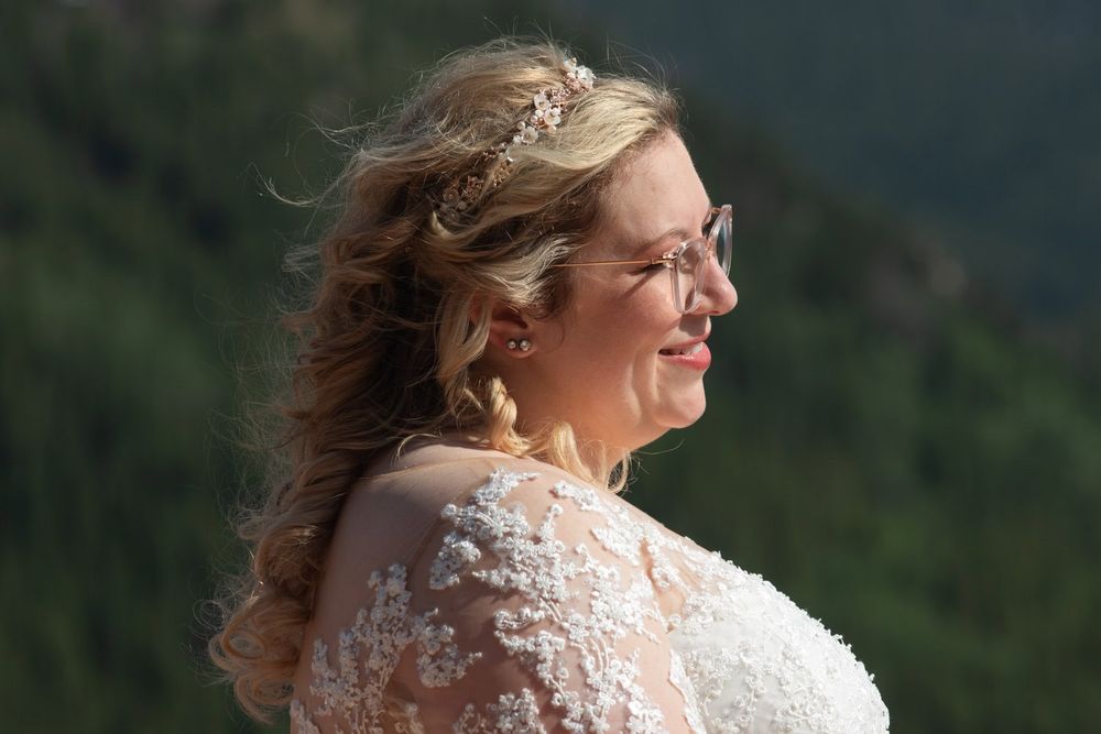 Bride in lace dress photographed against mountain backdrop with natural lighting.