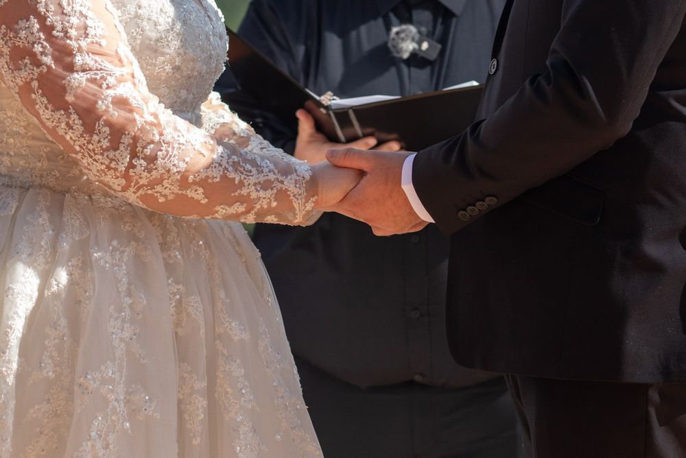 Wedding ceremony moment captured with bride in white lace dress and groom in dark suit.