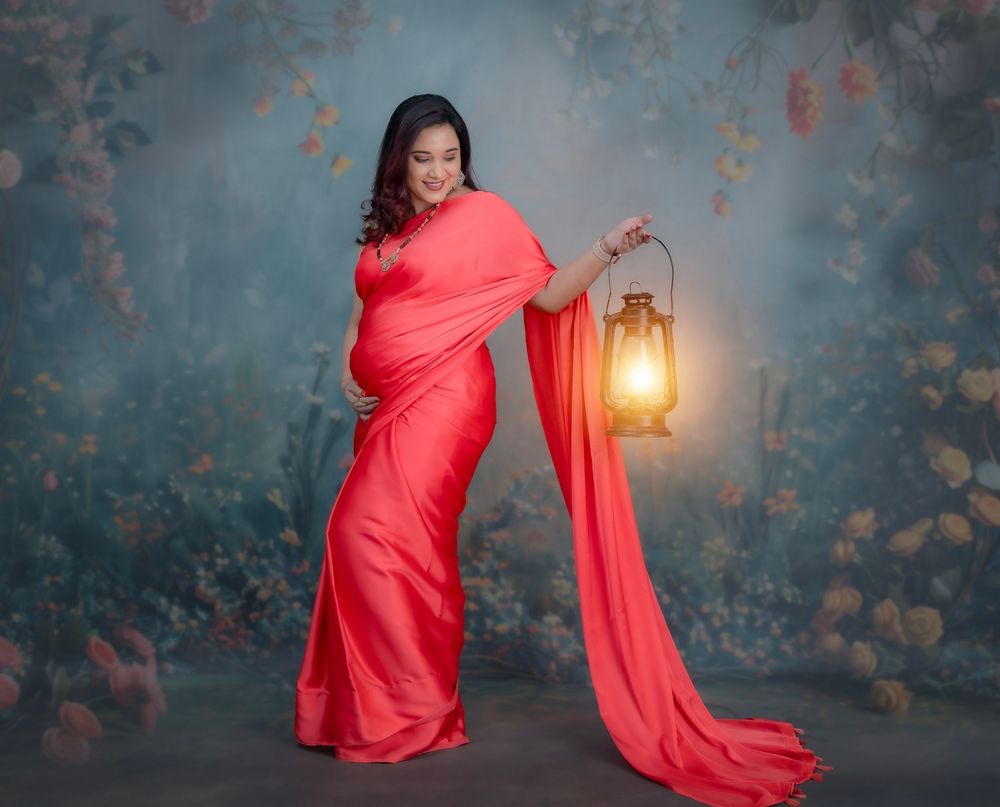 Pregnant woman posing in red drape with lantern during studio maternity photoshoot in Hyderabad