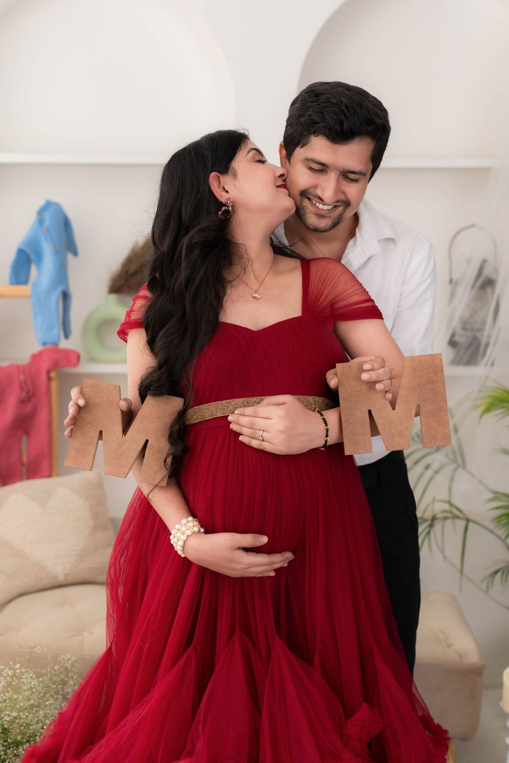 Couple posing together during studio maternity photoshoot, mother wearing red gown in Hyderabad