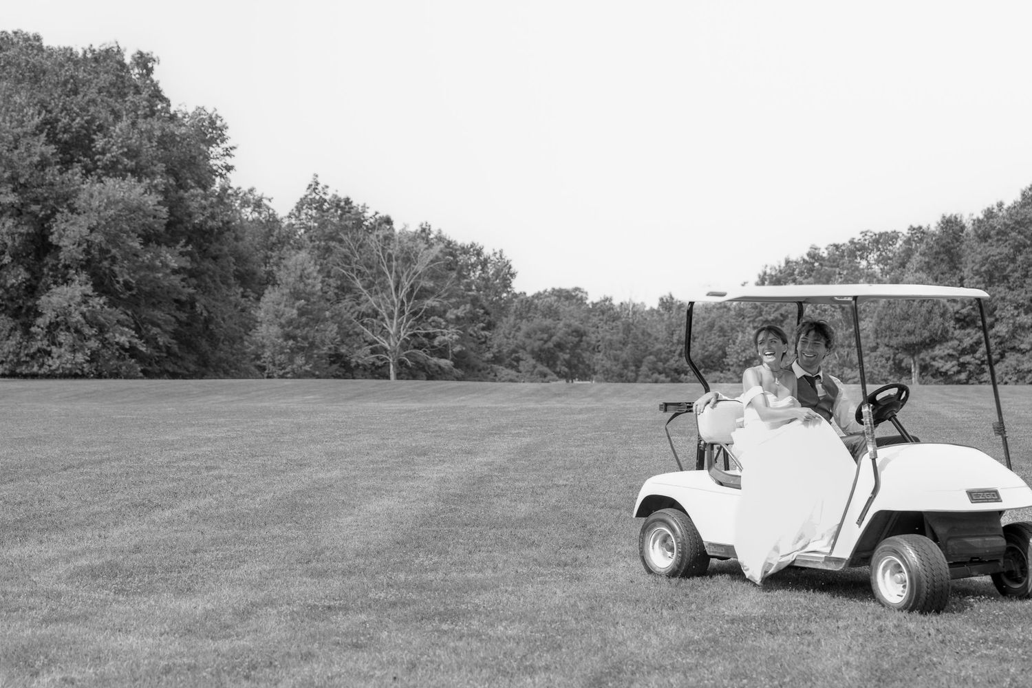 A white golf cart parked on a grassy field with trees in the background, captured in black and white.