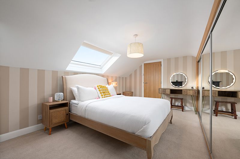 Modern attic bedroom with white walls, skylights, and wooden furniture creates a bright and airy sleeping space.