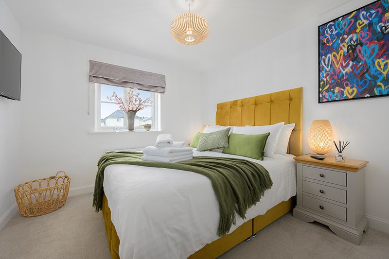 Modern bedroom features white walls, yellow accents, and natural light streaming through a window with a bamboo shade.