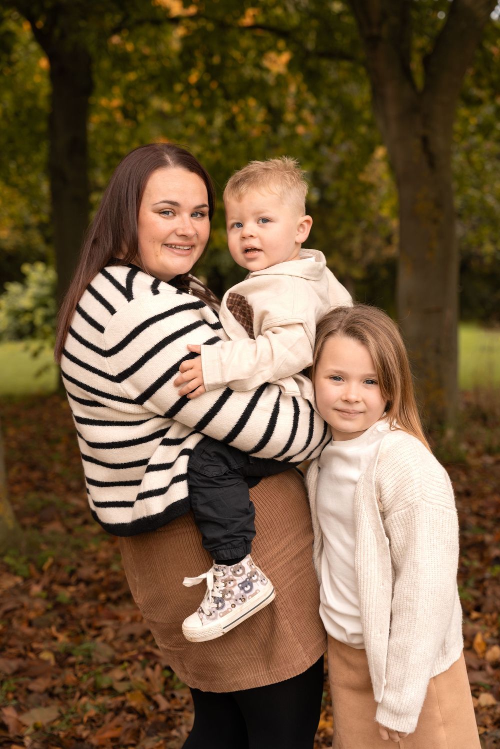 A family shares playful moments together on fallen autumn leaves in a park setting.