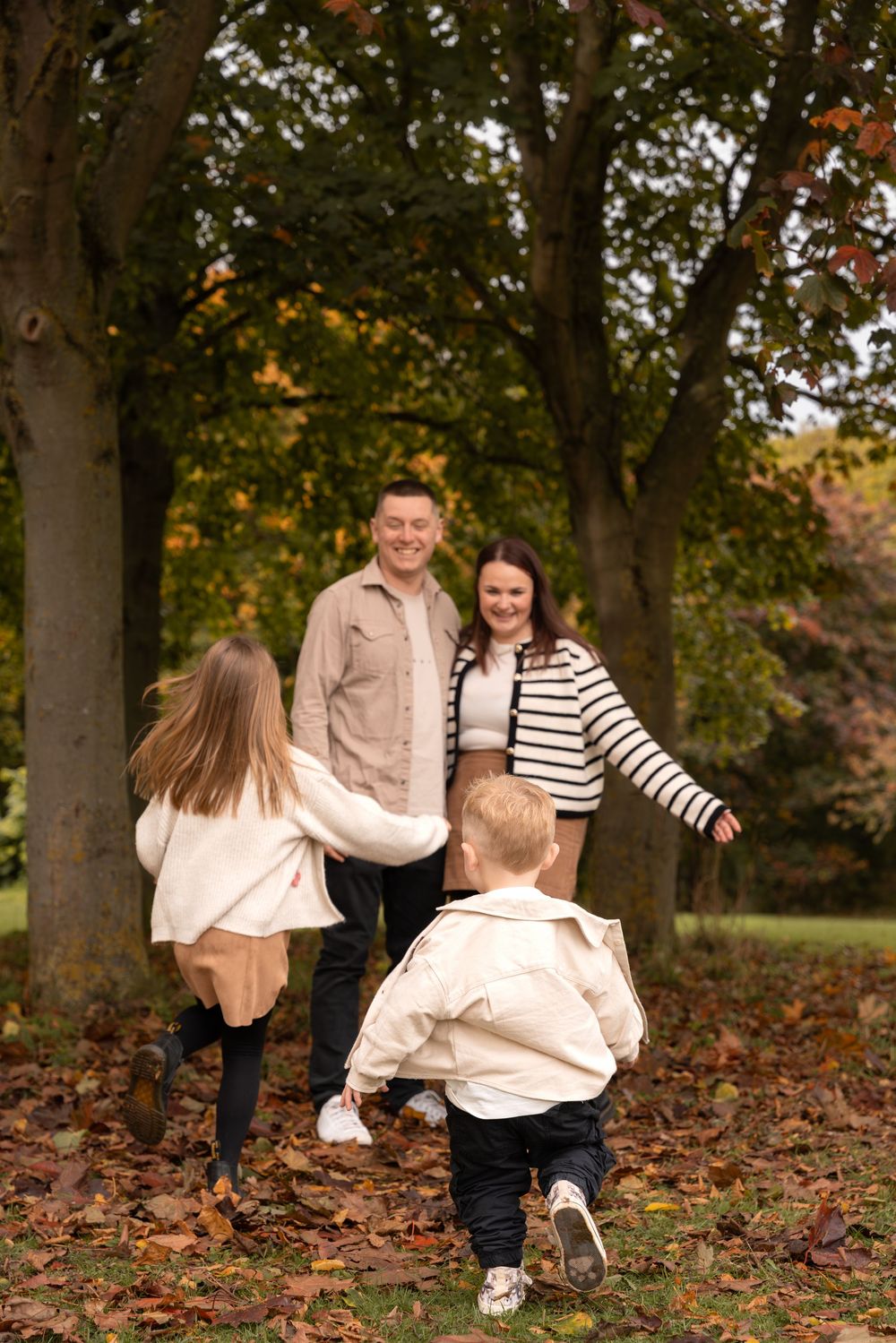 A family plays together in autumn leaves at a park during a fall photo session.