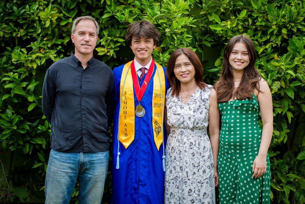 Graduation photo showing a group of four people standing together in front of green foliage outdoors.