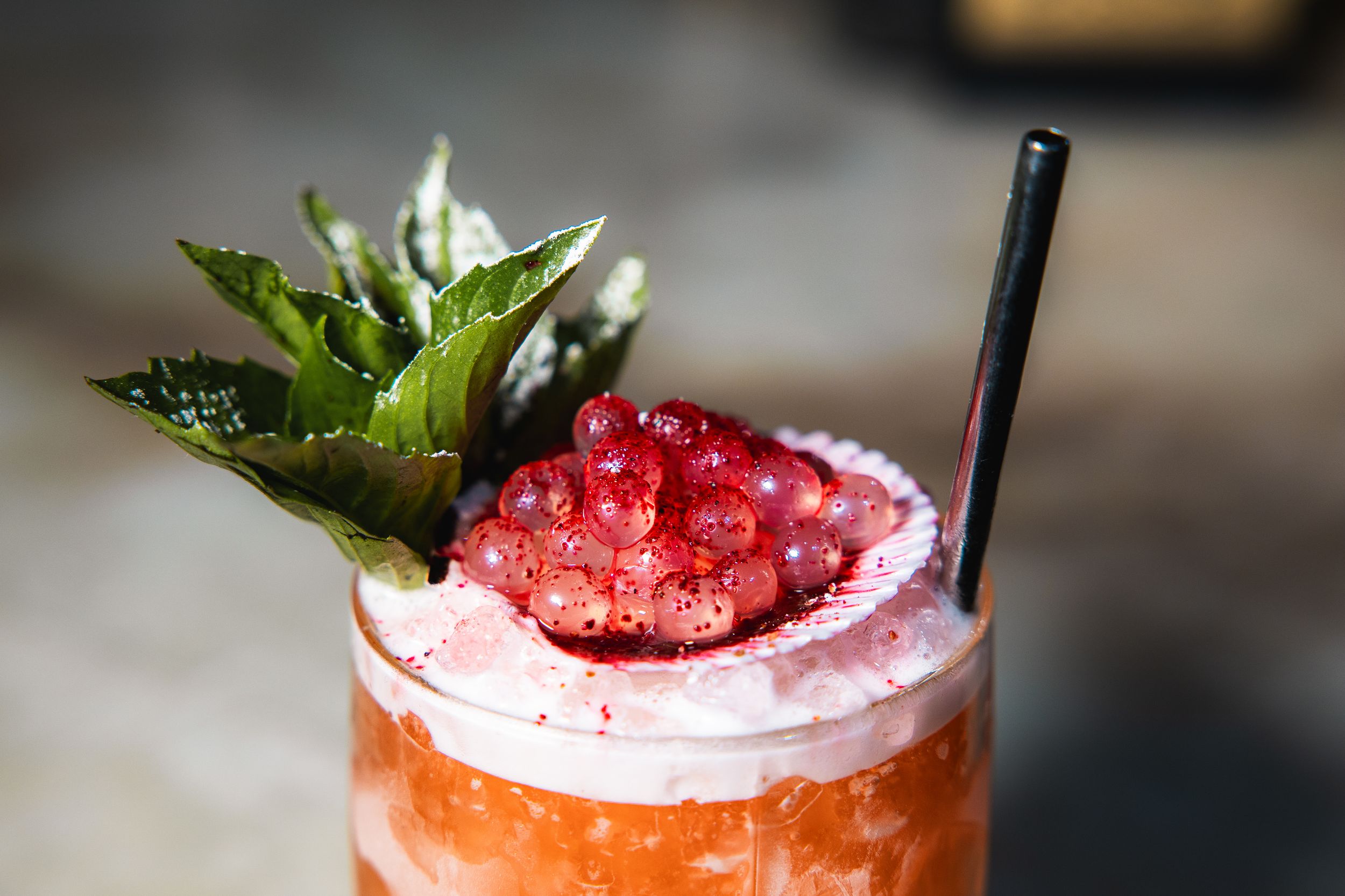 Vibrant tropical cocktail garnished with fresh raspberries, mint leaves and a black straw.