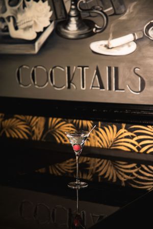Classic martini cocktail with garnish in elegant glass on dark bar counter with art deco palm leaf pattern.