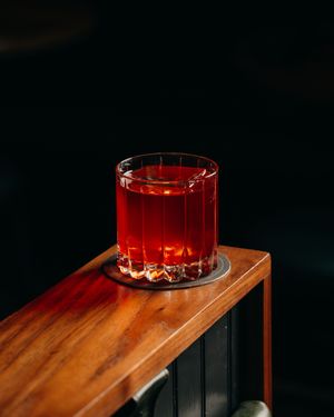 Red cocktail in a crystal glass sitting on a wooden table against black background.