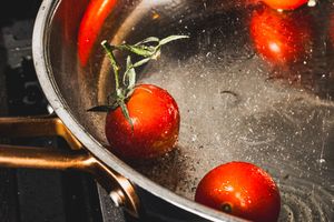 Fresh red tomatoes being washed in metal colander with dramatic lighting and water droplets.