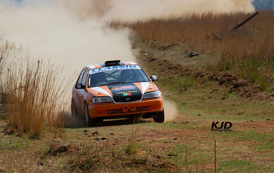 Rally cars race through a dusty off-road track while kicking up dirt and debris during a competition event.