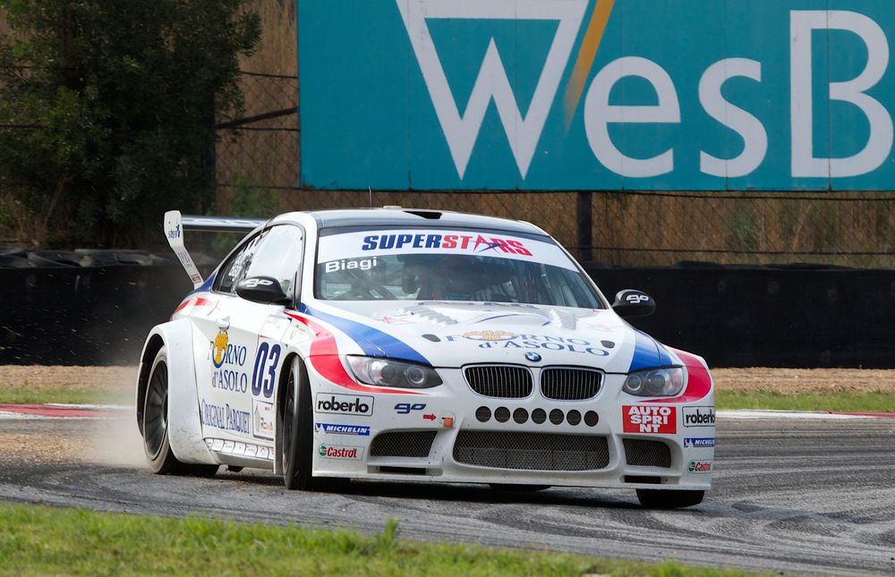 Racing car with sponsorship decals speeds around a track during a competitive motorsport event.