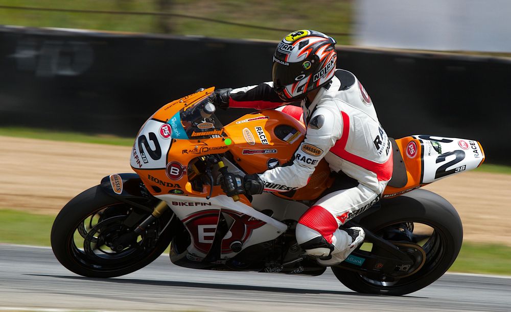 A motorcycle racer leans into a turn on an orange and white racing bike during a competition on a racetrack.