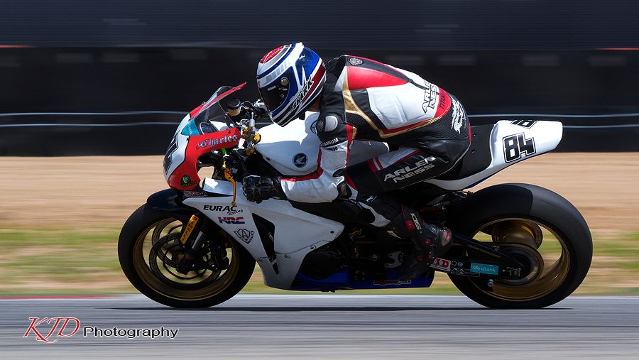 Racing motorcycles speed through a turn on a racetrack showing dynamic motion and skilled riding techniques.