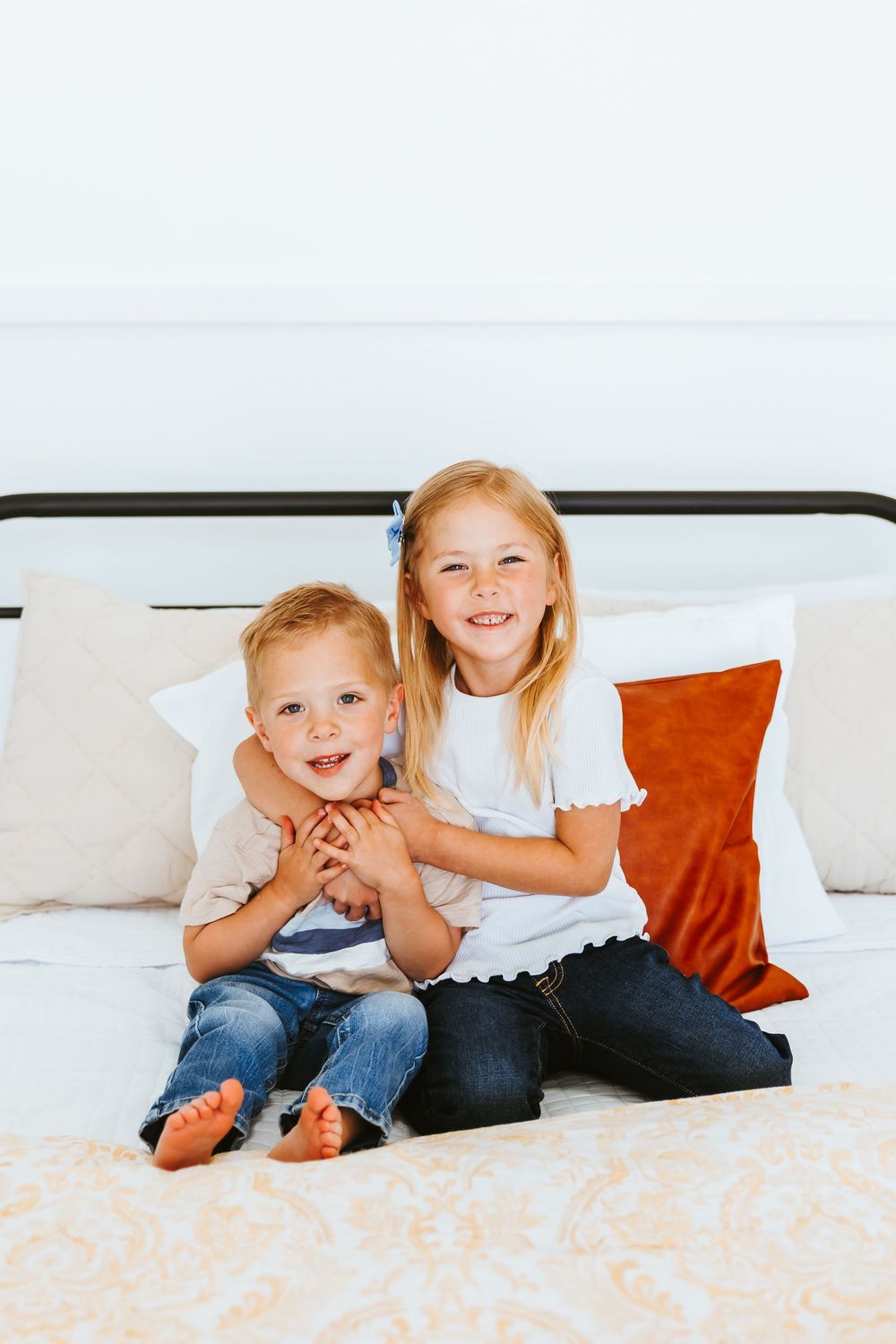 Children laughing and playing together on a white bed with orange accent pillows.