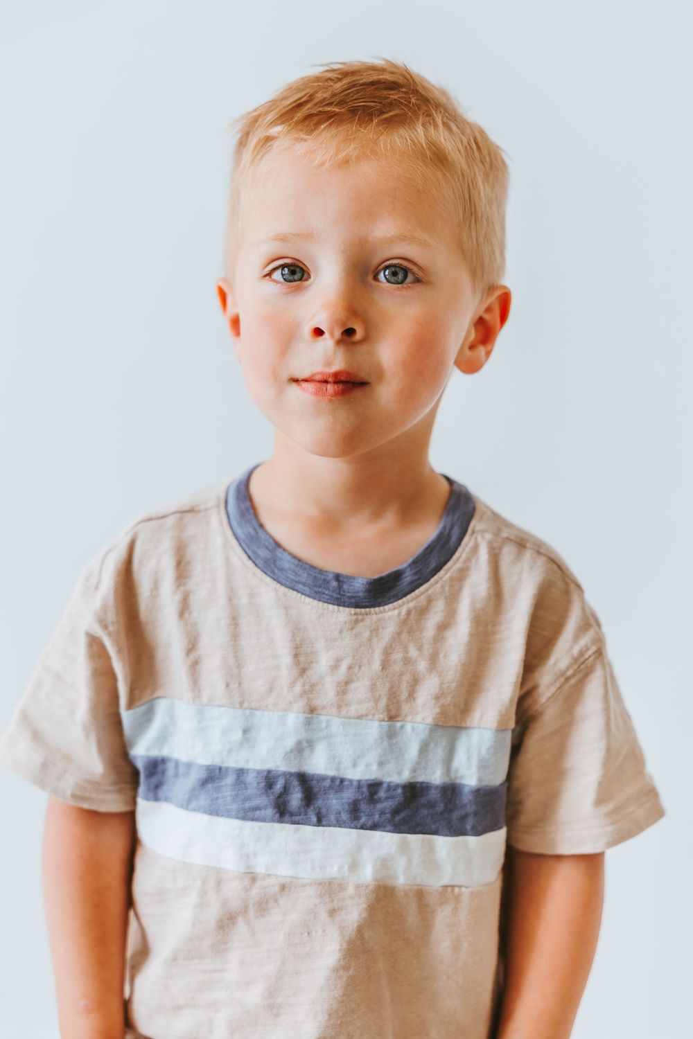 Three portrait shots showing a young child in a tan t-shirt with striped detail against a light background.