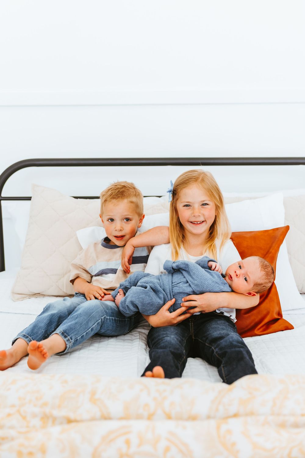 Children lying together on a white bed with orange pillows, displaying playful expressions.
