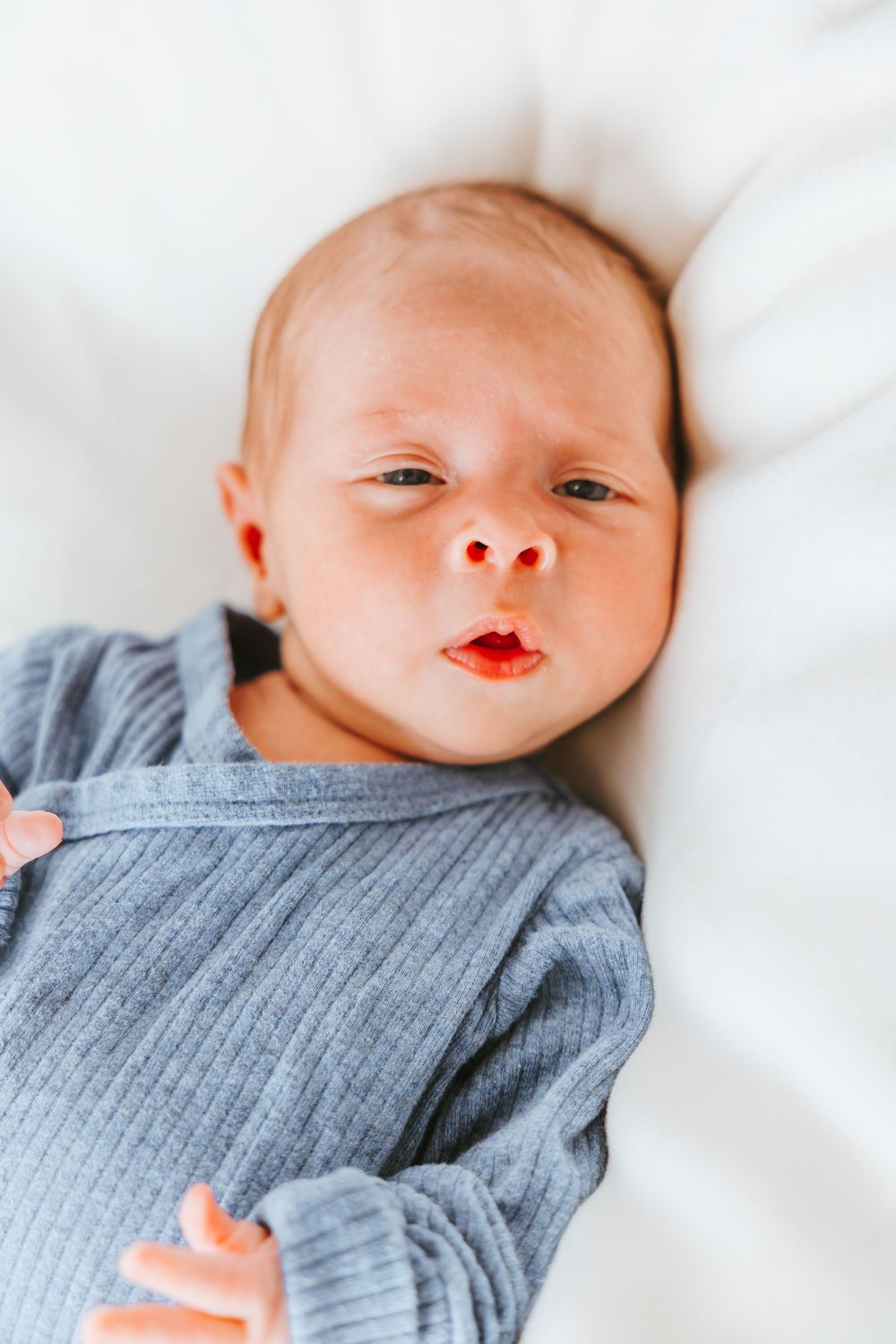 A series of close-up shots showing a newborn baby in a gray outfit lying on white bedding.