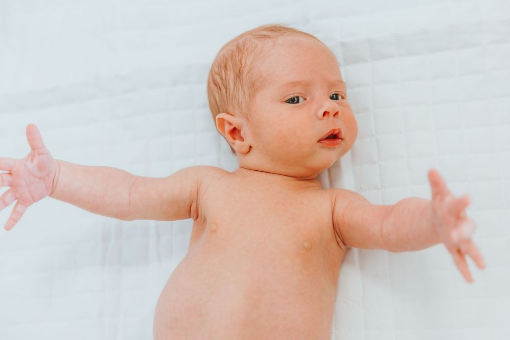 Newborn baby lying on white sheet with outstretched arms and peaceful expression.