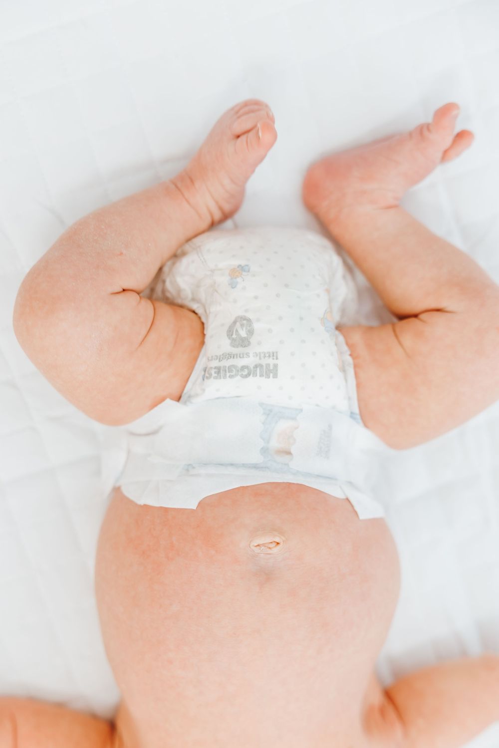 Close up view of baby legs and diaper against white bedding.