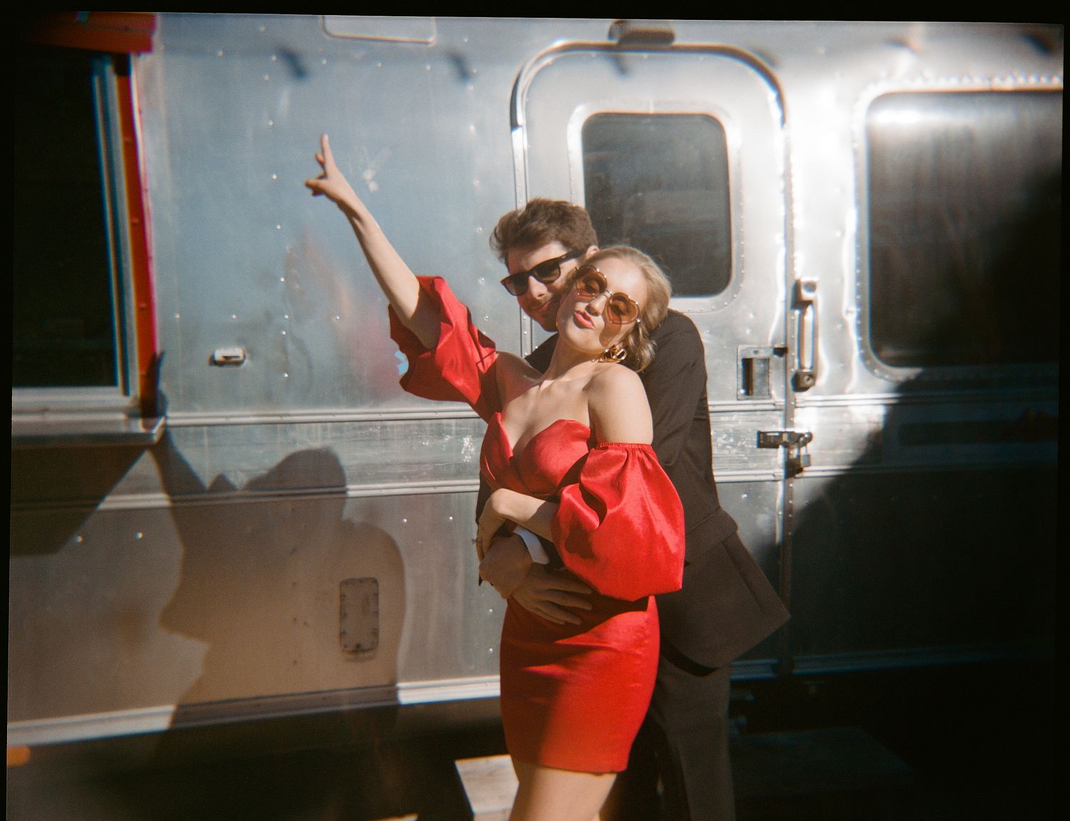 Retro-style photo of a couple posing playfully in front of an Airstream trailer.