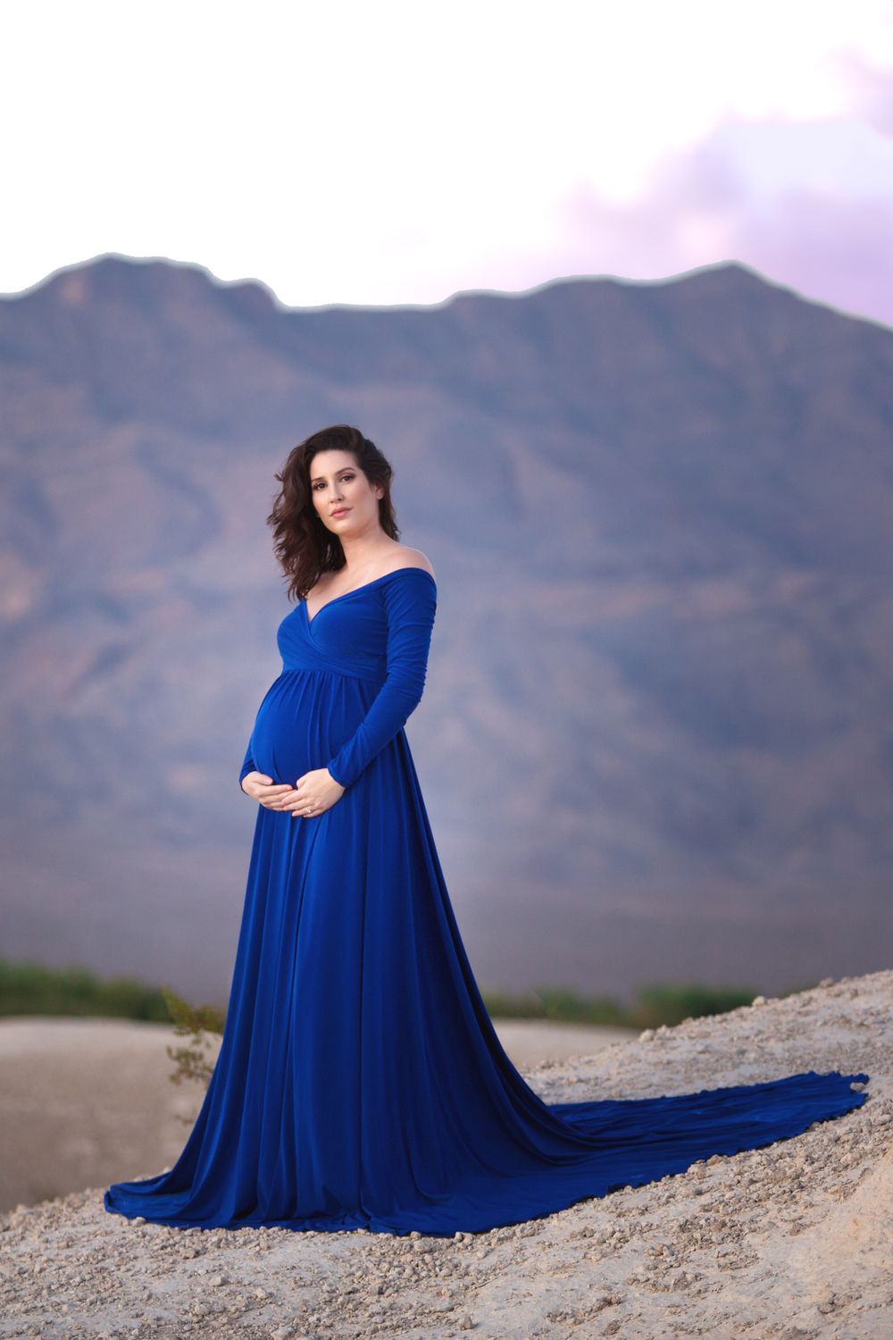 Elegant maternity portrait in a royal blue gown against mountain backdrop.