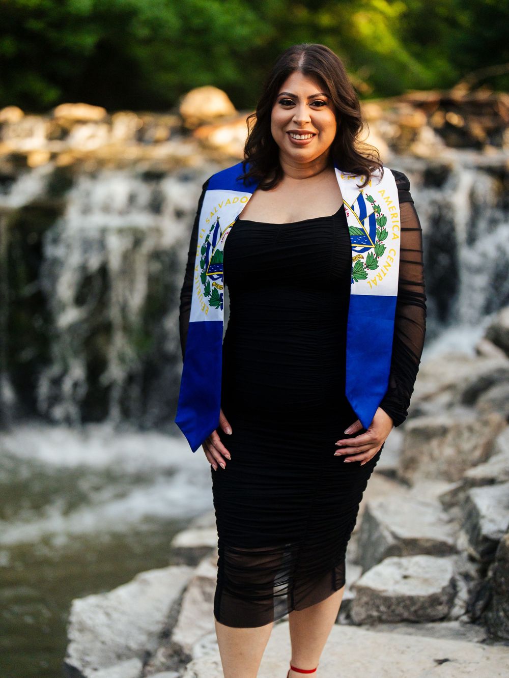 A scenic portrait session near a rocky waterfall backdrop with a person in a black and royal blue outfit.