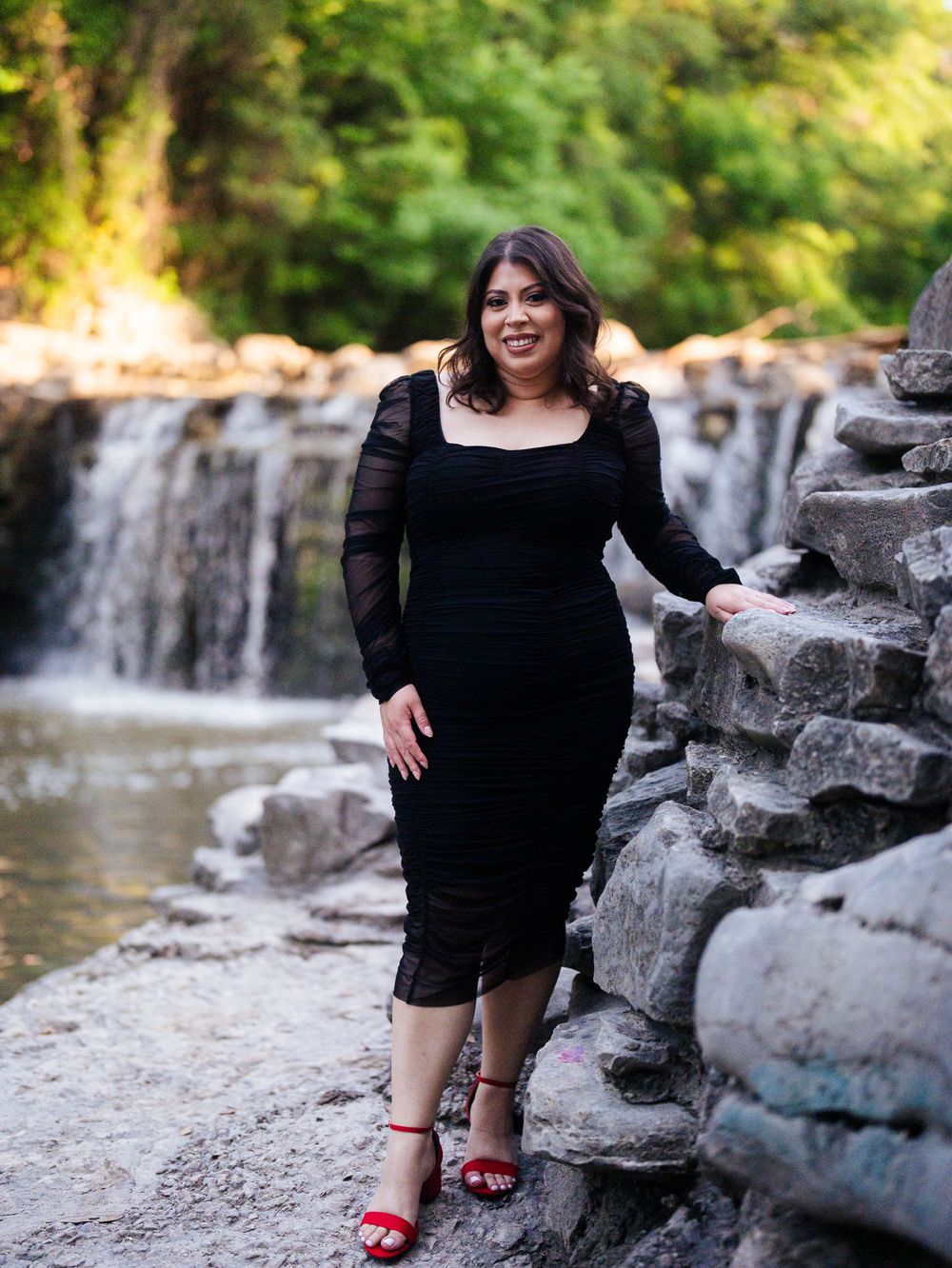 A woman in a black top and shorts poses on rock formations along a scenic waterfall stream.