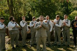 Groomsmen in gray suits line up for outdoor wedding photo.