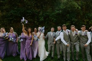 Wedding party in purple dresses and gray suits poses together outdoors.
