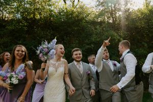 Joyful wedding party celebrates with raised arms in outdoor setting.
